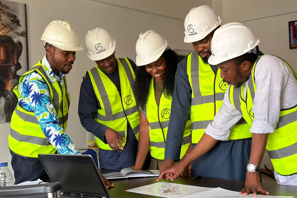 Contracting team in hard hats and safety vests reviewing project drawings around a desk in an office
