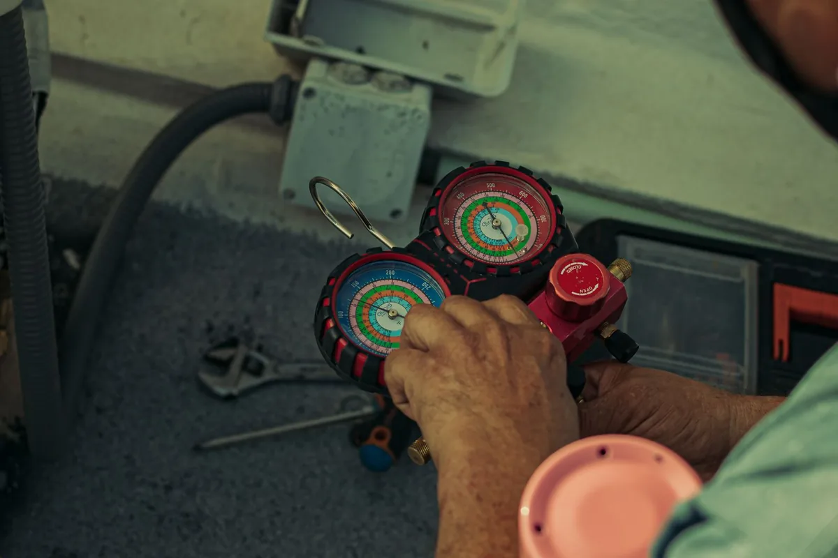 HVAC technician using a refrigerant manifold gauge set while servicing an air-conditioning unit