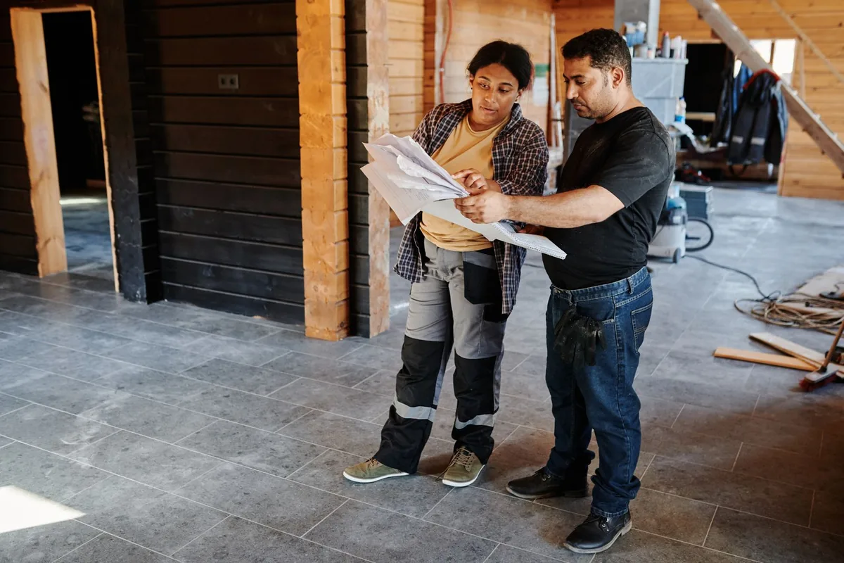 Two site workers reviewing project drawings inside a building under construction
