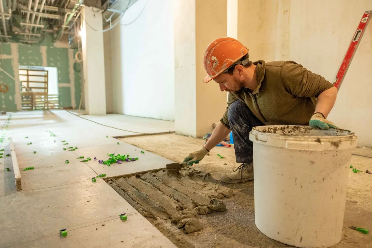 Tiler in safety gear laying floor tiles with spacers during an interior renovation
