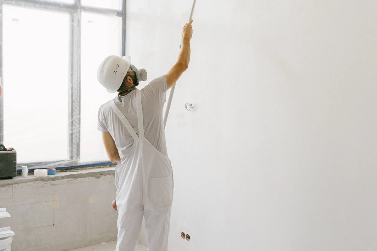 Painter in white uniform applying a roller coat of paint to an interior wall