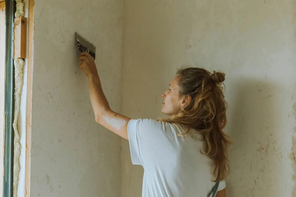 Worker applying and smoothing plaster across an interior wall with a steel trowel