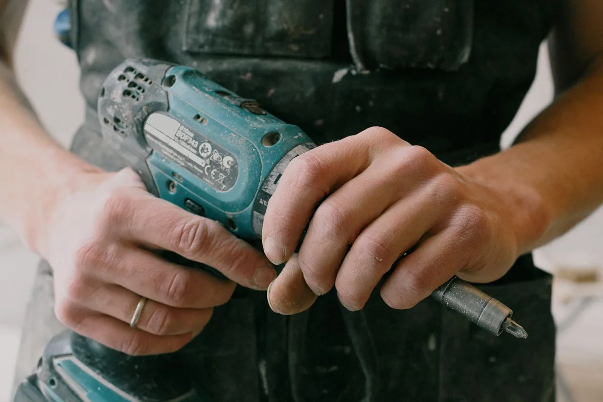 Maintenance technician in uniform using a cordless drill during a repair call-out in an apartment