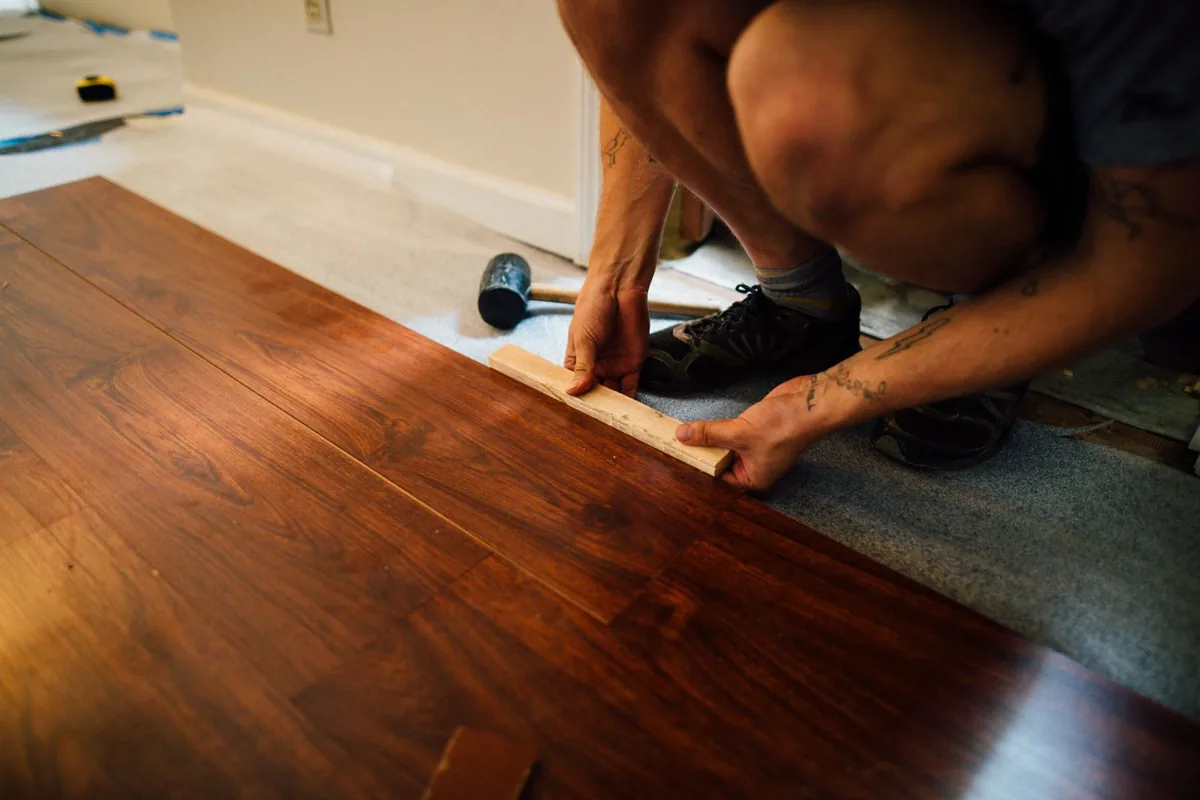 Installer tapping engineered wood flooring planks into place with a mallet during a renovation